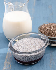 Chia seeds, milk, and Chia seed pudding close up on blue wooden background, vertical banner