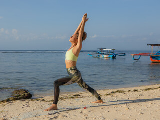 Young woman practicing Virabhadrasana I, Warrior I Pose. Hands in namaste mudra. Yoga retreat. Healthcare concept. Thomas beach, Bali, Indonesia