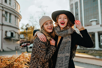 Enchanting woman in checkered scarf laughing on city background. Indoor photo of spectacular girls...
