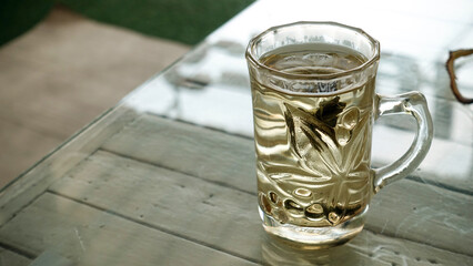 Hot tea in clear glass on a wooden table with glass in the morning.
