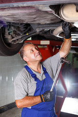 portrait of elderly mechanic engaged in car repair in modern auto workshop