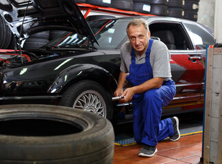 Fototapeta na wymiar Mature man car mechanician changing car wheel in auto repair shop..