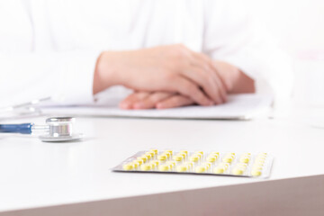 Doctor talking about pills during doctor's appointments. Small yellow pills in focus. Blurred doctor's hands. Healthcare and medicine concept. Selling drugs.