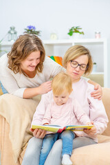 Obraz premium Female couple sitting on the sofa of their front room with their child, readding her a book