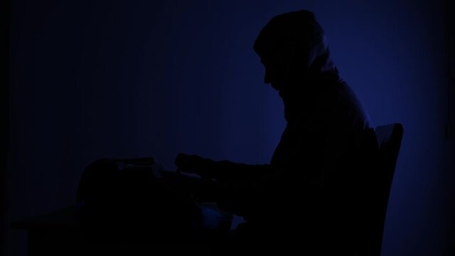 Silhouette of a mysterious man typing on a vintage typewriter, alone in a dark room.