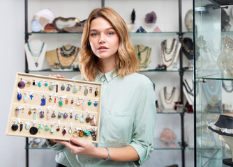 Elegant young saleswoman showing various pendants from colorful natural gemstones in jewelry store