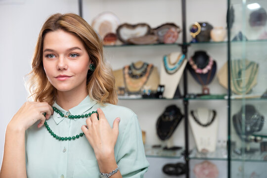 Young interested woman trying on elegant necklace from green jadeite in modern jewelry shop