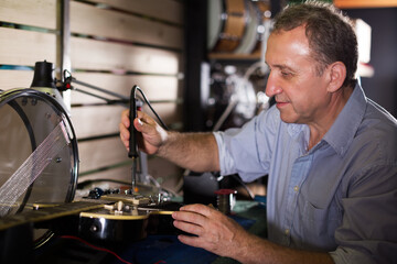 mature serious male is repairing music instruments in music store.