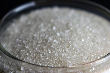 Top View Closeup White Sugar Crystals in a Open Transparent Glass jar On isolated Black Background