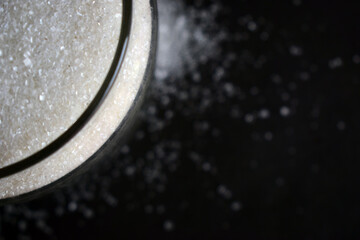 Top View Closeup White Sugar Crystals in a Open Transparent Glass jar On isolated Black Background