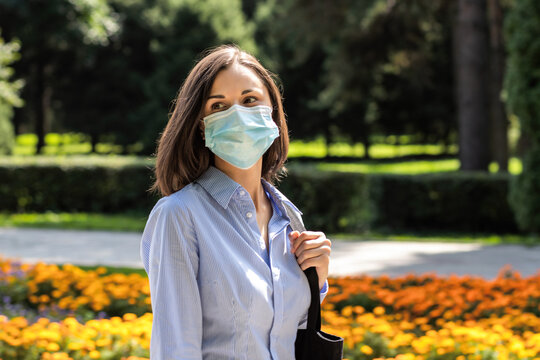 Beautiful Young Woman Walking In A Summer Park Wearing A Protective Medical Mask.