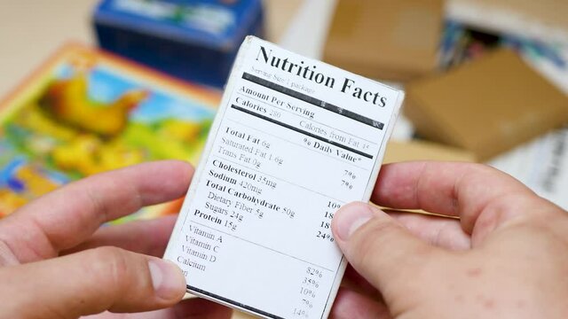 Hold in hands food label with ingredients on paper box. Shopping and nutrition. Affixed to product on which printed information about item. Critical information pertinent to contents used in product