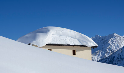 The roof of an house or hotel covered by massive quantity of fresh snow after heavy snowfall. Mountain and winter contest. Italian alps