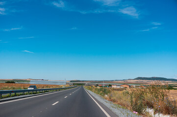 By car on the highway past the fields. Color photo