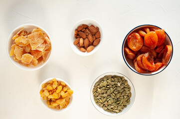 Different dried fruits and nuts in white plates on a light background. A healthy snack. Winter vitamins. View from above. 
