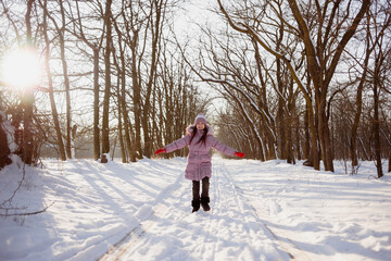 Fototapeta na wymiar A little girl stands on the road in a snowy forest. Winter games for children. Outdoor entertainment concept.