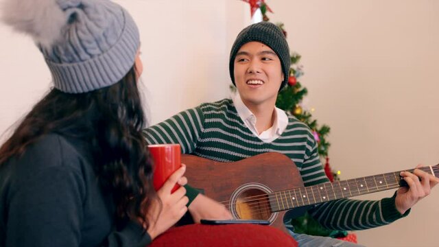 Asian happy young family couple sitting in decorated christmas living room on winter holidays together and singing while playing the guitar. Holiday celebration concept, 4K Resolution, Slow motion