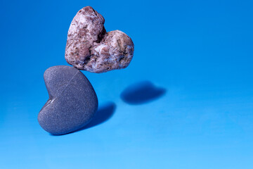 Levitation. Falling stones in the shape of a heart on a blue background. Stone hearts of different...