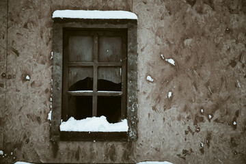 An old window on the wall of an abandoned house. Snow on the ground.