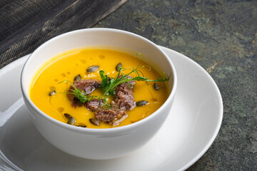 Pumpkin soup with chopped beef and seeds in a white bowl on a stone background, close up