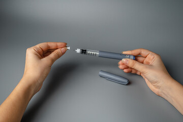 young woman holds a syringe for insulin. Diabetes is a disease of the endocrine system. Syringe on a gray background.