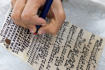 A writer's hand practices decorating letters from a Torah scroll written on parchment in Hebrew,...