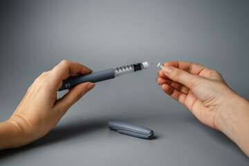 A young woman holds a syringe for insulin. Diabetes is a disease of the endocrine system. Syringe on a gray background.