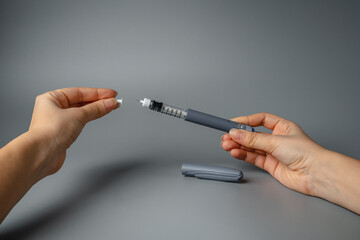 Young woman holds an insulin pen syringe and an insulin pump in her hands. Diabetes is a disease of the endocrine system. Syringe on a gray background.