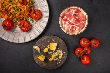 Pasta with prosciutto ham, cherry tomatoes, parmesan and pesto sauce on dark graphite background, top view, copy space