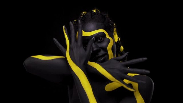 Face art. Dancing woman with black and yellow body paint. Young african girl with colorful bodypaint. An amazing afro american model with yellow makeup. Closeup face.