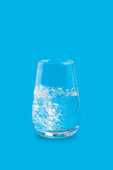 Transparent clear tasteless, odorless, and colorless water with bubbles in single drinking glass against bright vibrant blue background. Vertical orientation image