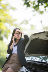 Asian business woman sad waiting for help by a broken car. Use a mobile phone to call the mechanic.