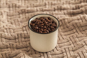 White cup full of coffee beans on knitted sweater