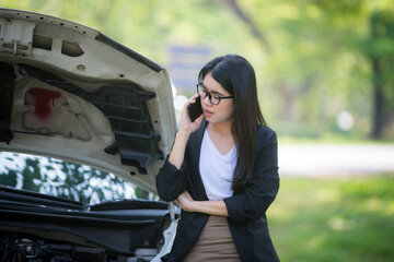 Asian business woman sad waiting for help by a broken car. Use a mobile phone to call the mechanic.