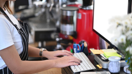 Fototapeta na wymiar Close up view female entrepreneur in an apron using computer at counter bar in coffee shop.
