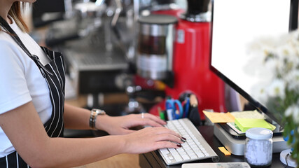 Close up view female entrepreneur in an apron using computer at counter bar in coffee shop.