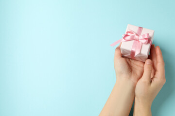 Female hands holding gift box with pink ribbon on blue background