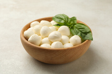 Bowl with mozzarella and basil on white textured background, close up