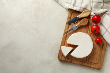 Cutting board with camembert cheese, tomato, fork and towel on white textured background