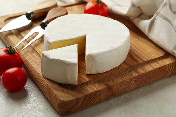Cutting board with camembert cheese, tomato, fork and towel on white textured background
