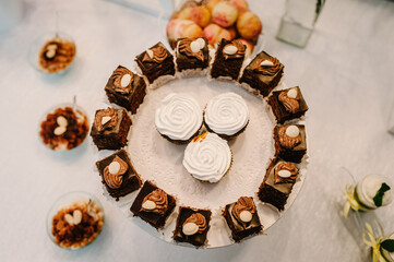 Delicious sweet chocolate and vanilla cakes in a plate on a background festive sweet table with baking. Top view.