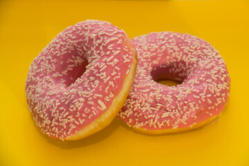 two sweet donuts with pink icing on a yellow background