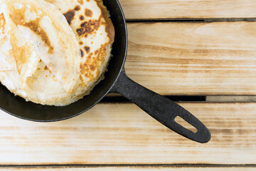 Black pan filled with thin pancakes on a wooden background