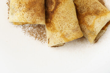 A close-up of rolled pancakes sprinkled with cocoa on a white plate