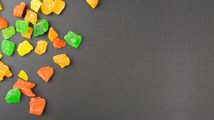 Colored candied fruits on a black background with copy space. Multi-colored pieces of dried fruits.