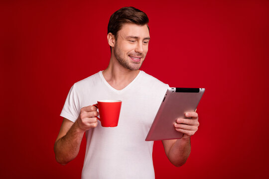 Photo portrait smiling guy holding mug with tea reading on tablet isolated vivid red color background