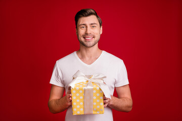 Portrait of handsome cheerful person hands hold giftbox toothy smile isolated on maroon color background