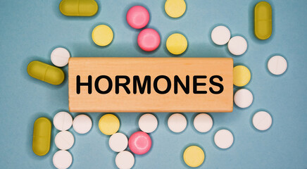 HORMONES written on wooden block on a blue background among multicolored pills. Medical concept