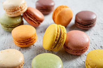 Multicolored macaroons or macarons - delicious French small cakes lying in a mess on a gray table, selective focus