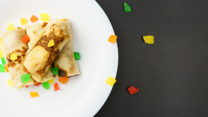 Top view of white plate with thin pancakes stuffed with candied fruits on black background